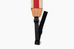 Close-up of a camera strap with a beige and red striped fabric section, tan leather trim, and a black adjustable webbing strap with plastic buckles, shown on a plain white background.
